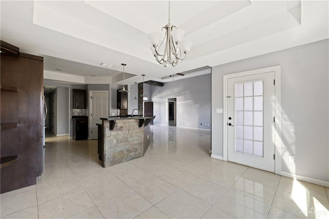 kitchen featuring sink, hanging light fixtures, a kitchen breakfast bar, a notable chandelier, and a tray ceiling