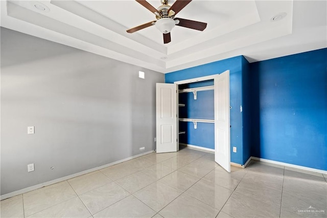 unfurnished bedroom with a raised ceiling, light tile patterned floors, ceiling fan, and a closet