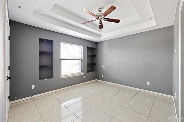 tiled empty room featuring a raised ceiling, built in features, and ceiling fan