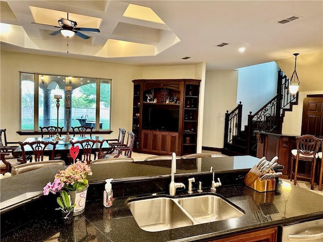 kitchen with sink, dark stone counters, hanging light fixtures, coffered ceiling, and ceiling fan