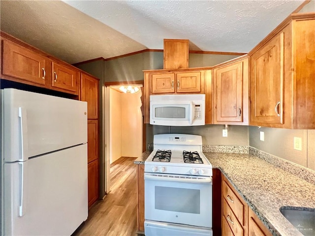 kitchen with lofted ceiling, white appliances, light stone countertops, light wood-type flooring, and ornamental molding