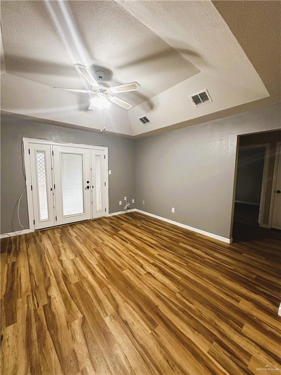 unfurnished bedroom with a raised ceiling, ceiling fan, hardwood / wood-style floors, and a textured ceiling