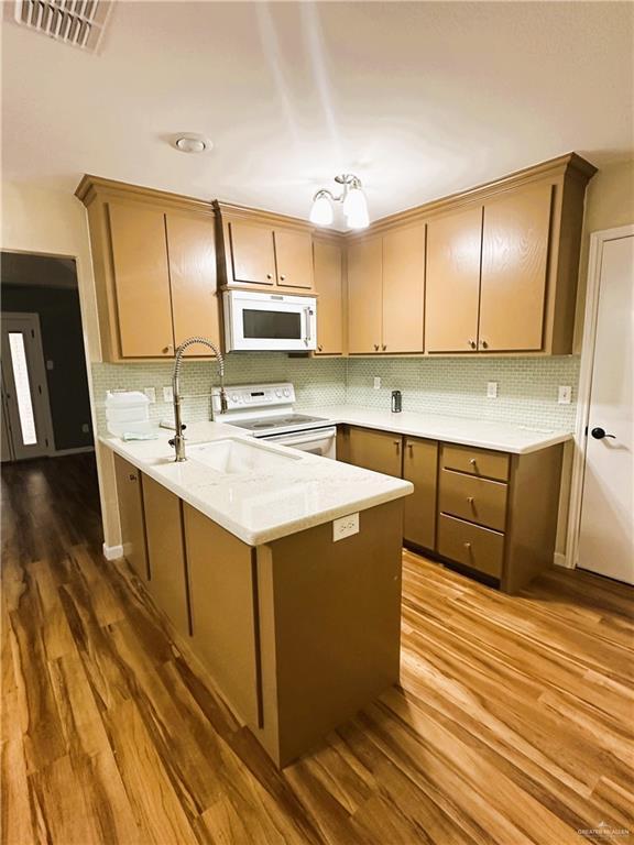 kitchen with white appliances, wood-type flooring, kitchen peninsula, and sink