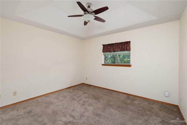 carpeted empty room with a raised ceiling and ceiling fan