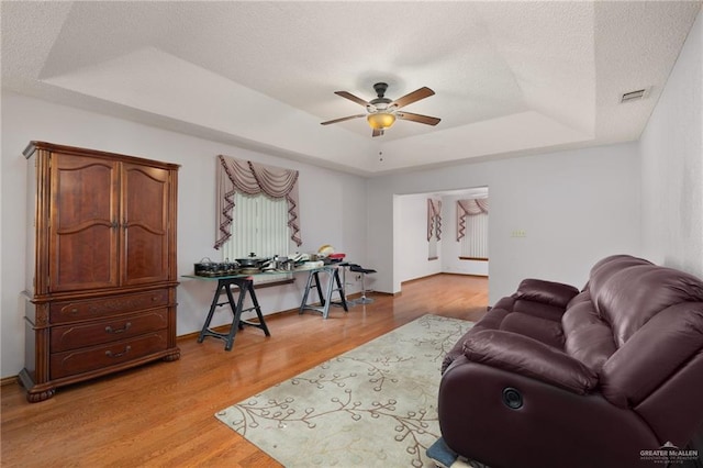 living room with ceiling fan, light hardwood / wood-style floors, a textured ceiling, and a tray ceiling