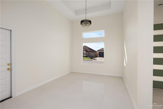 tiled empty room featuring a chandelier and a tray ceiling