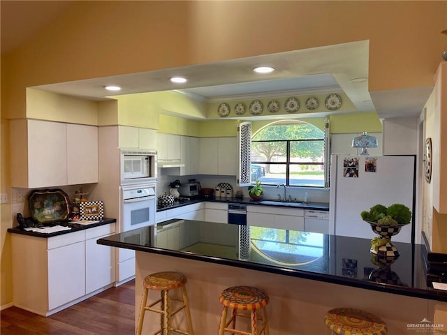 kitchen featuring a breakfast bar, white cabinetry, sink, dark hardwood / wood-style flooring, and white appliances