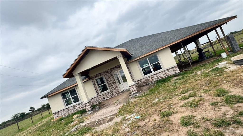 view of front of home with a carport, stone siding, stucco siding, and fence