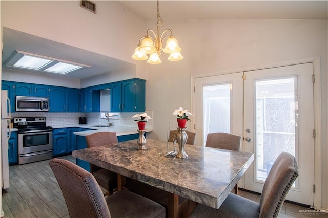 kitchen with appliances with stainless steel finishes, sink, backsplash, blue cabinets, and decorative light fixtures