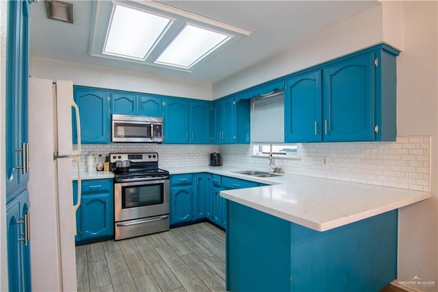 kitchen with appliances with stainless steel finishes, sink, blue cabinetry, kitchen peninsula, and decorative backsplash