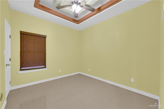 empty room featuring ceiling fan, a raised ceiling, and light tile patterned floors