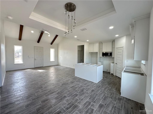 kitchen featuring a tray ceiling, stainless steel microwave, visible vents, and wood finish floors