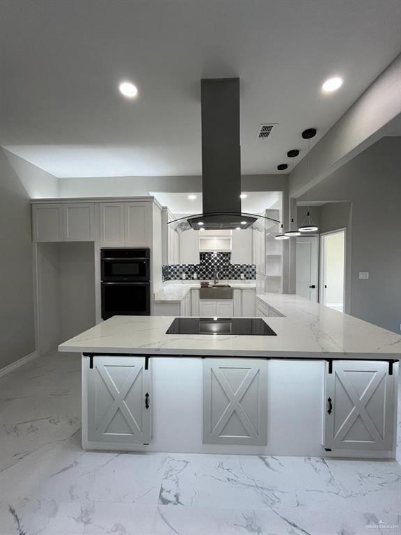 kitchen with light stone counters, island range hood, tasteful backsplash, and black appliances