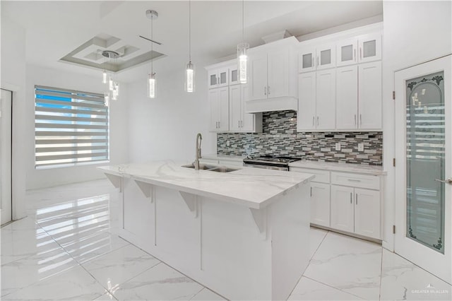 kitchen with sink, hanging light fixtures, white cabinets, and a center island with sink