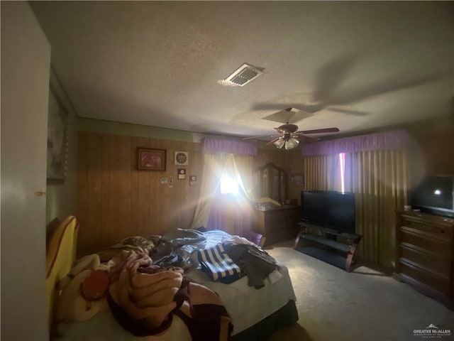 carpeted bedroom with a textured ceiling, ceiling fan, and wood walls