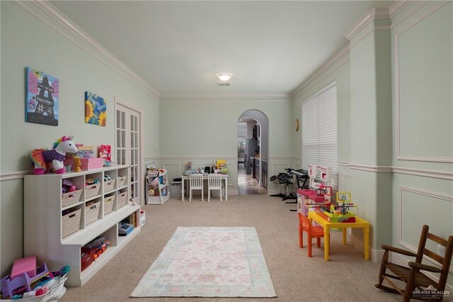 game room featuring carpet floors, ornamental molding, wainscoting, and arched walkways