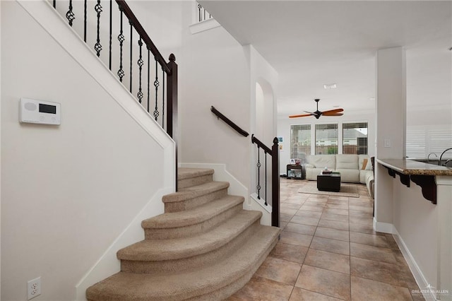 stairs with ceiling fan, baseboards, tile patterned flooring, and arched walkways