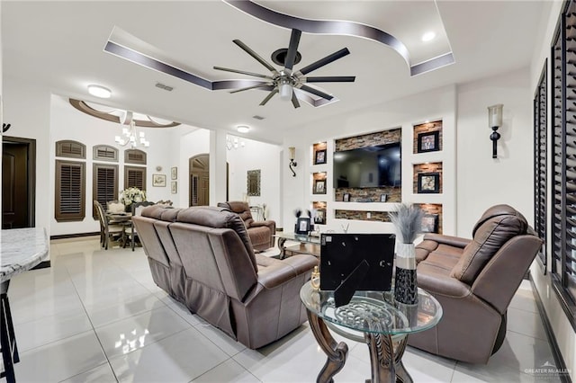 living room featuring a tray ceiling, a fireplace, light tile patterned floors, visible vents, and ceiling fan with notable chandelier