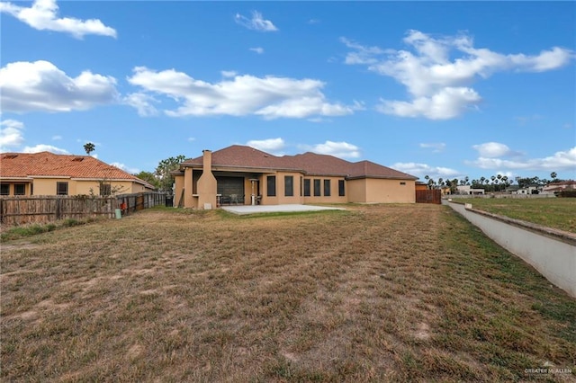 rear view of house featuring a lawn, a patio area, fence, and stucco siding