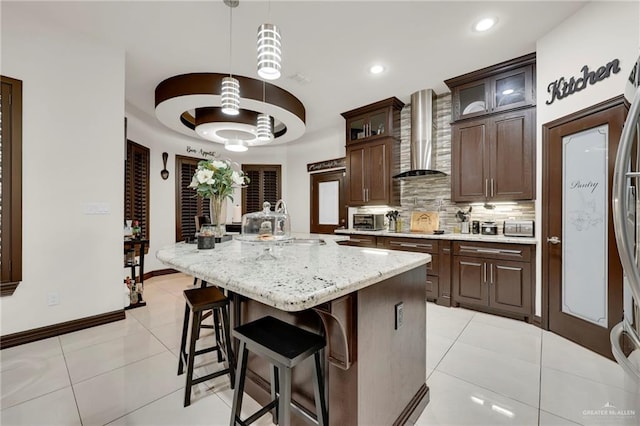 kitchen with light tile patterned floors, backsplash, a sink, wall chimney range hood, and an island with sink