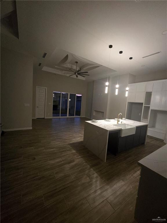 kitchen with sink, ceiling fan, hanging light fixtures, light stone countertops, and a center island with sink