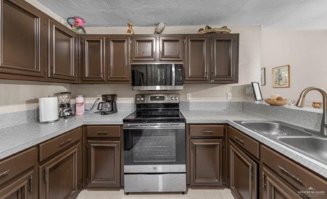 kitchen with sink, light tile patterned floors, appliances with stainless steel finishes, dark brown cabinets, and a textured ceiling