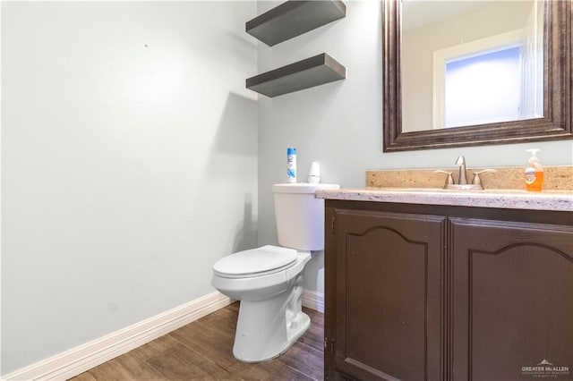 half bathroom with vanity, baseboards, toilet, and wood finished floors