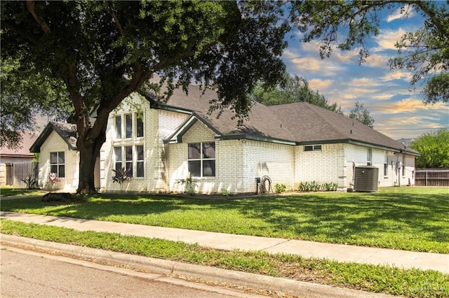 view of front of home featuring a front yard, brick siding, fence, and central AC unit