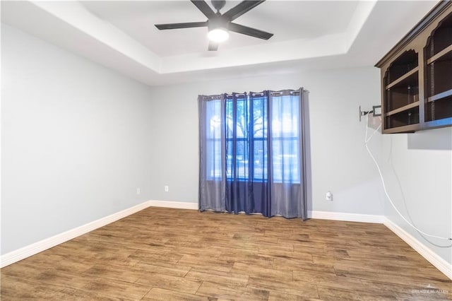 unfurnished room with a tray ceiling, ceiling fan, wood finished floors, and baseboards