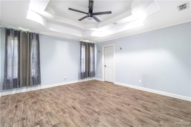 spare room with visible vents, baseboards, a raised ceiling, a ceiling fan, and wood finished floors