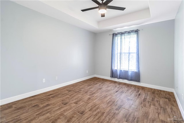 empty room featuring a raised ceiling, wood finished floors, ceiling fan, and baseboards