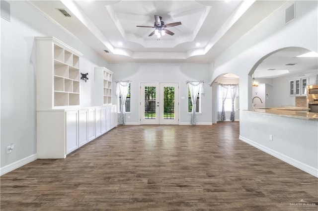 unfurnished living room featuring arched walkways, a ceiling fan, visible vents, dark wood-style flooring, and a raised ceiling