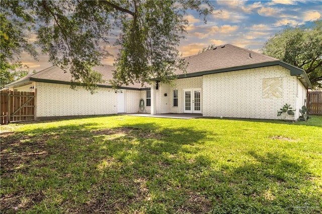 back of house with a yard, a fenced backyard, a patio area, brick siding, and french doors