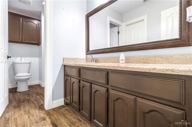 bathroom with toilet, wood finished floors, vanity, and baseboards