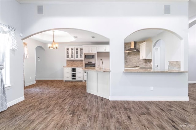 kitchen with white cabinets, a tray ceiling, wall chimney exhaust hood, appliances with stainless steel finishes, and a sink