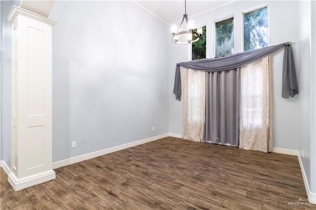 empty room featuring a chandelier, baseboards, ornamental molding, and wood finished floors