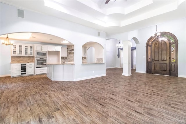 unfurnished living room with visible vents, a tray ceiling, baseboards, and wood finished floors
