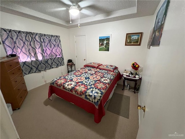 carpeted bedroom with a textured ceiling, a tray ceiling, and ceiling fan