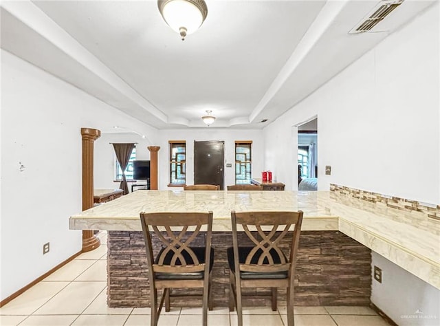 dining area with a raised ceiling, light tile patterned floors, and ornate columns