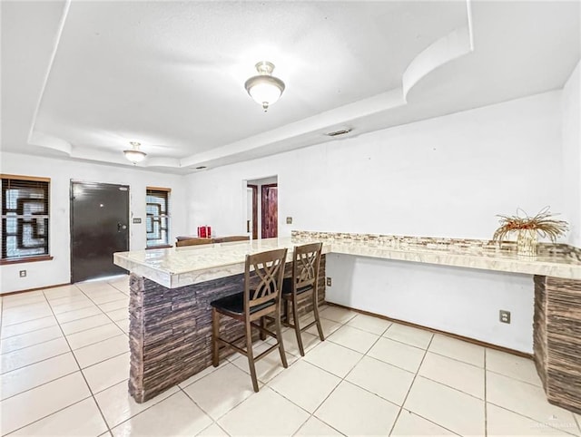 kitchen with a raised ceiling, kitchen peninsula, black fridge, and light tile patterned flooring