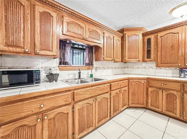 kitchen featuring sink, tile countertops, a textured ceiling, decorative backsplash, and light tile patterned floors