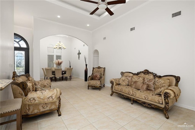 living area with a high ceiling, ceiling fan with notable chandelier, light tile patterned flooring, crown molding, and a tray ceiling