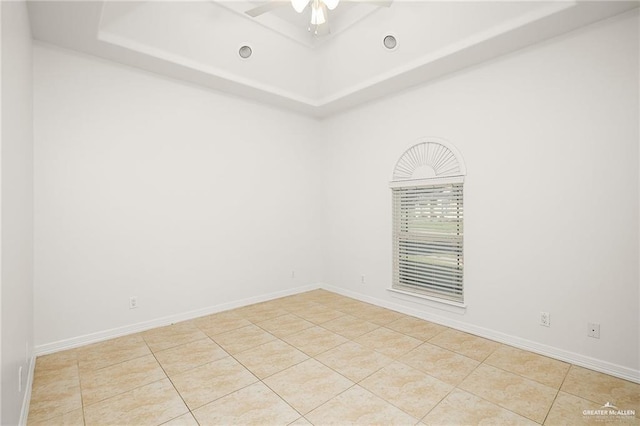 empty room with a raised ceiling, light tile patterned floors, and ceiling fan