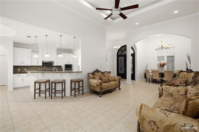 living room featuring a tray ceiling, light tile patterned floors, ornamental molding, and ceiling fan with notable chandelier