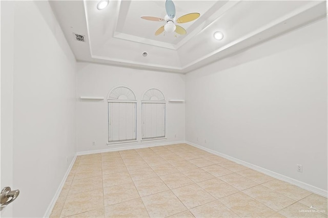 spare room featuring a raised ceiling, ceiling fan, and light tile patterned flooring