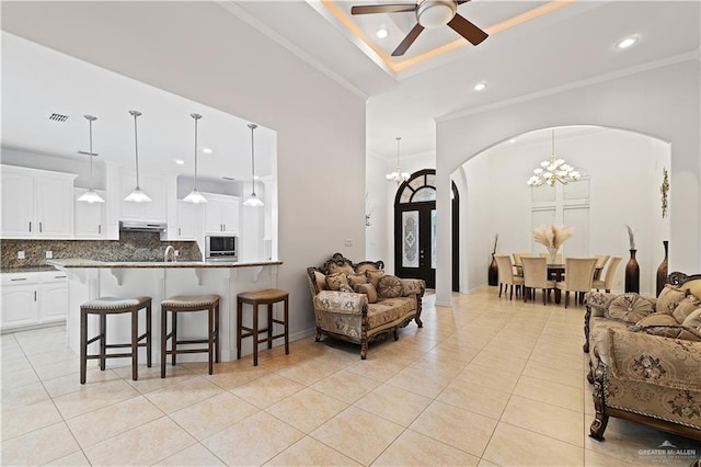 tiled living room featuring a raised ceiling, ceiling fan with notable chandelier, ornamental molding, and a towering ceiling