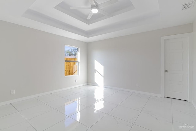 empty room with ceiling fan and a tray ceiling