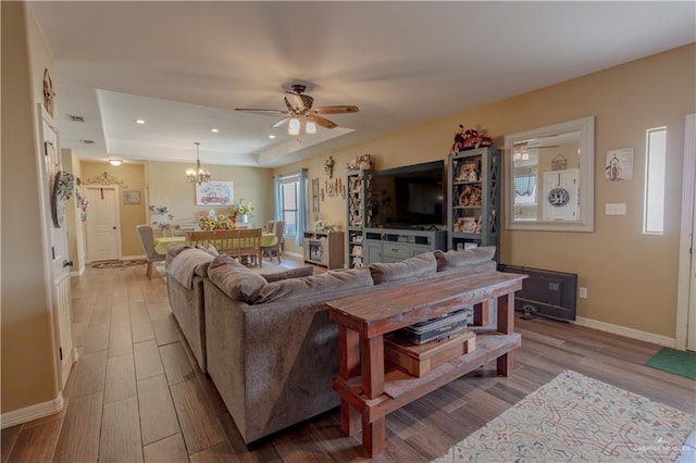 living room featuring baseboards, a tray ceiling, ceiling fan with notable chandelier, recessed lighting, and wood finished floors