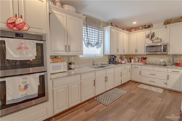 kitchen with light stone counters, light wood finished floors, a sink, stainless steel appliances, and white cabinets