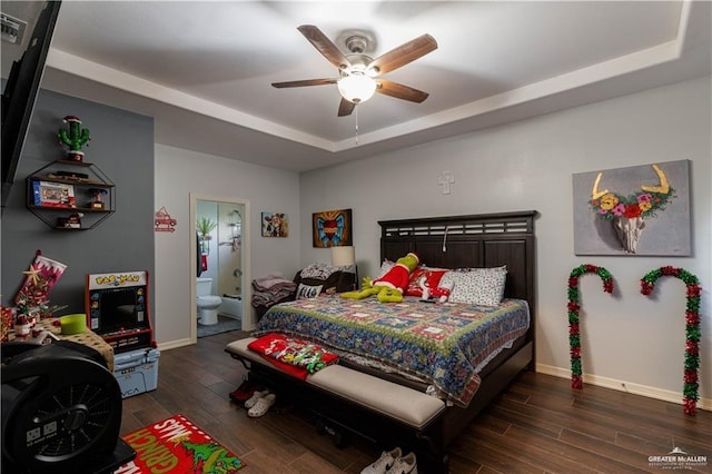 bedroom featuring ensuite bath, a raised ceiling, wood finished floors, and baseboards